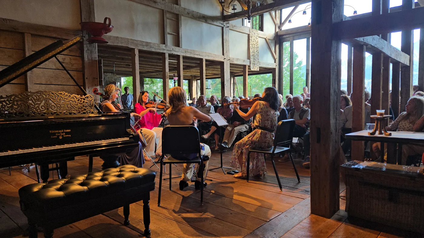 Audience inside the Mai Home during a MusicFest performance — open barn windows looking out to the mountains